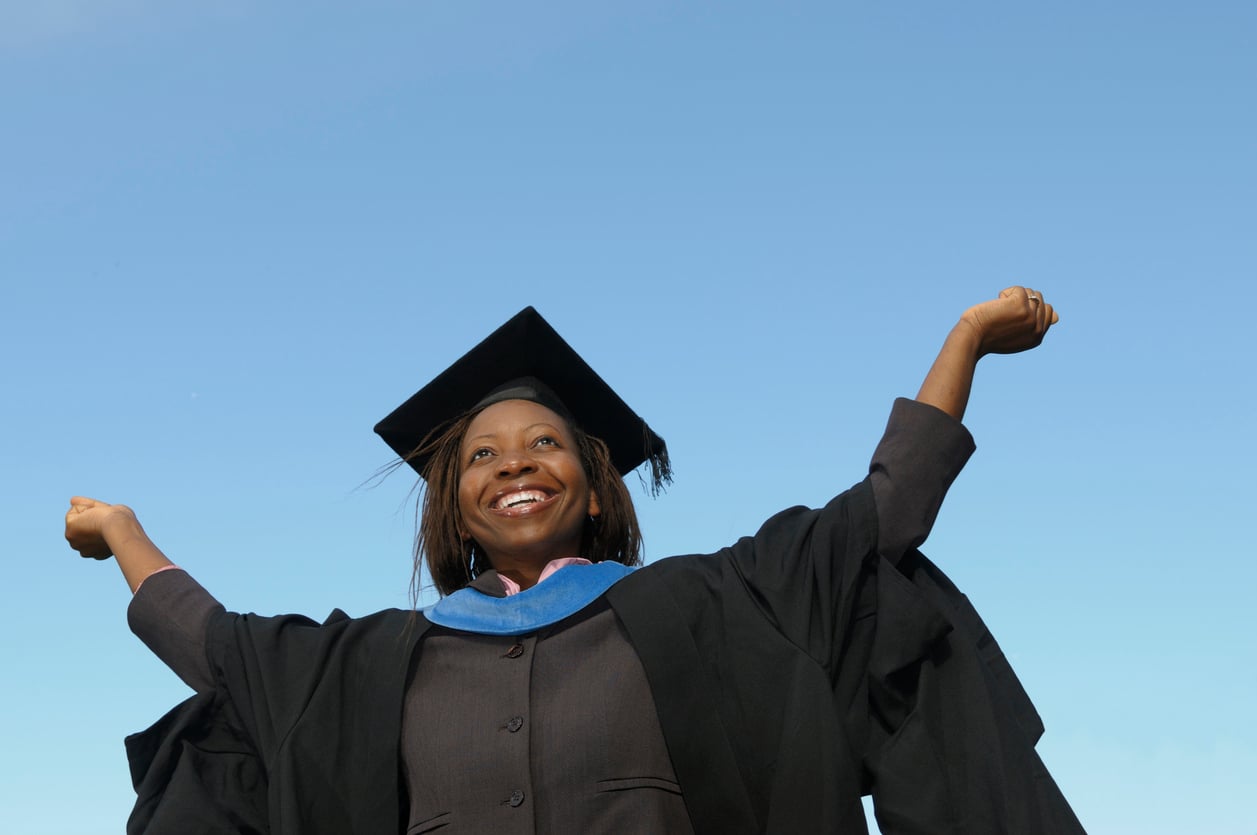 New grad wearing cap and gown triumphantly raises arms
