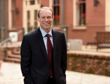 Adam J. MacLeod poses in a black suit and red tie.