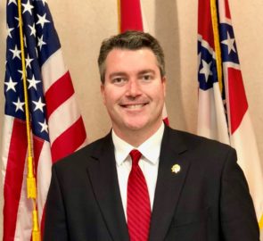 Josephy Willoughby poses in a suit in front of the American flag.